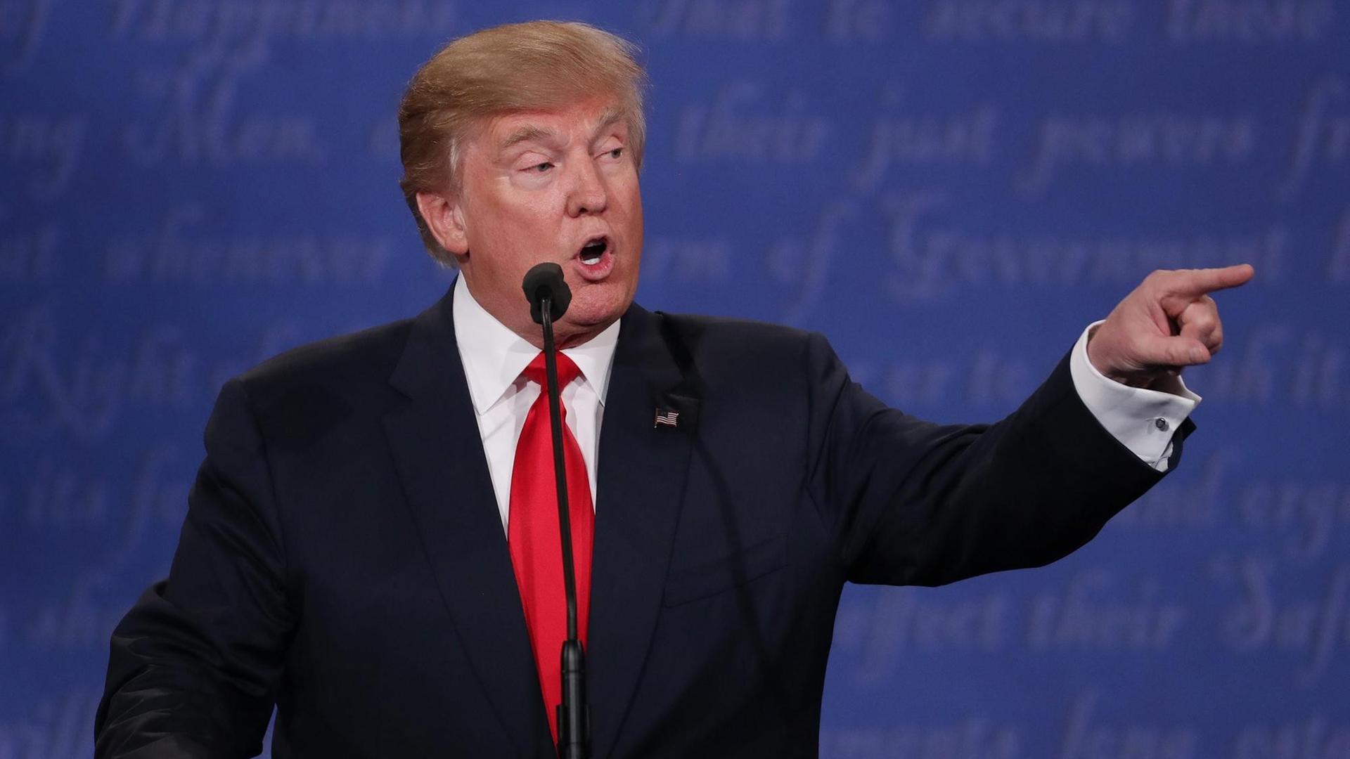 Trump steht an einem Rednerpuklt und zeigt mit dem Finger zu seiner Linken