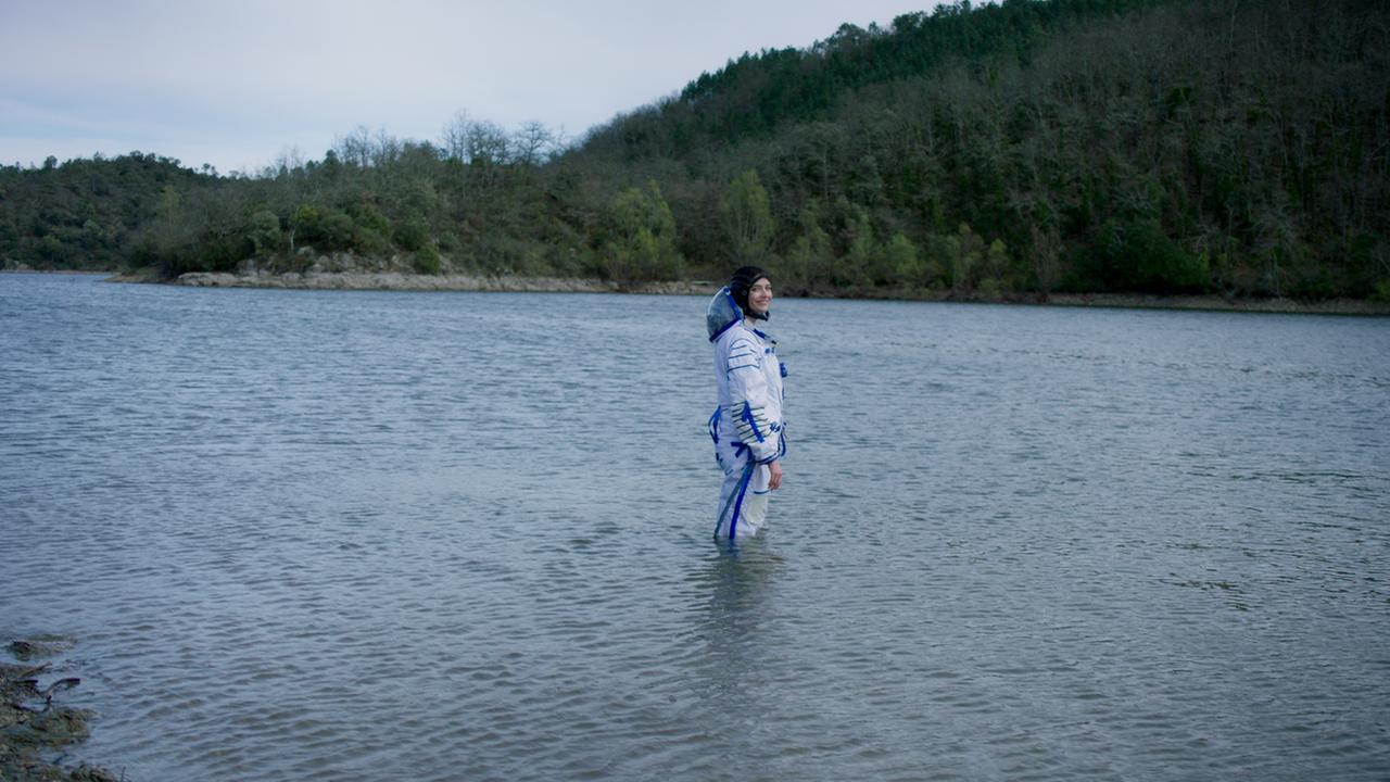 Eva Green steht in Astronautenmontur in einem See und lächelt zur Kamera