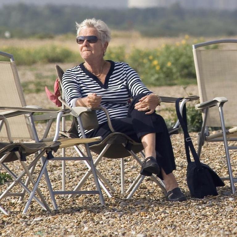 Eine Frau sitzt am Strand von Aldeburgh in Großbritannien auf einem Klappstuhl und genießt die Sonne, aufgenommen im Juli 2005.