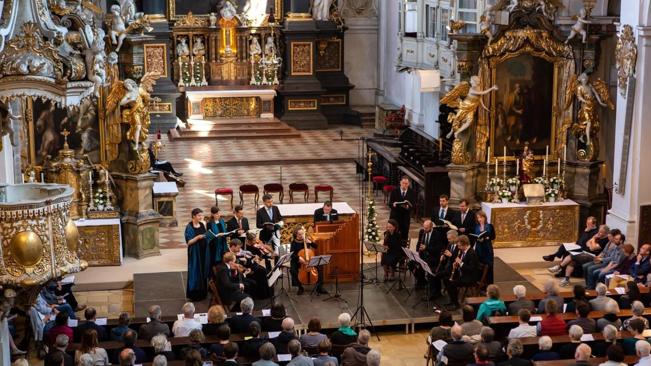 Das Ensemble Vox Luminis in der im Barock neu ausgestalteten Basilika St. Emmeran in Regensburg, die Sängerinnen und Sänger gruppieren sich um die Instrumente im Halbkreis.