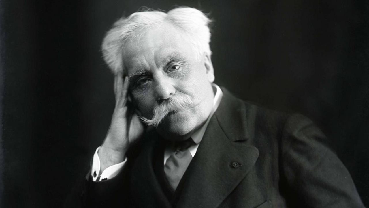 Schwarz-weiß Fotografie des Komponisten Gabriel Fauré (1845-1924), er hat weiße Haare und einen weißen Schnurbart, er trägt eine schwarze Anzugjacke mit breitem Revers, ein weißes Hemd und einen dunklen Schlips, er schaut in dei Kamera und hat seinen Kopf auf die rechte Hand gestützt