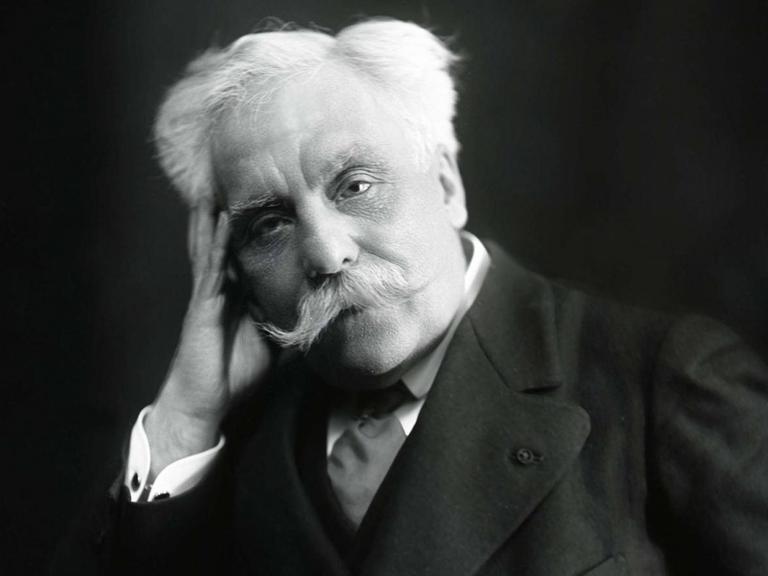 Schwarz-weiß Fotografie des Komponisten Gabriel Fauré (1845-1924), er hat weiße Haare und einen weißen Schnurbart, er trägt eine schwarze Anzugjacke mit breitem Revers, ein weißes Hemd und einen dunklen Schlips, er schaut in dei Kamera und hat seinen Kopf auf die rechte Hand gestützt