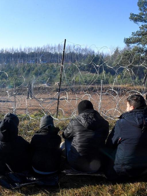 Fünf Personen sitzen an der belaruissisch-polnischen Grenze vor einem Stacheldrahtzaun