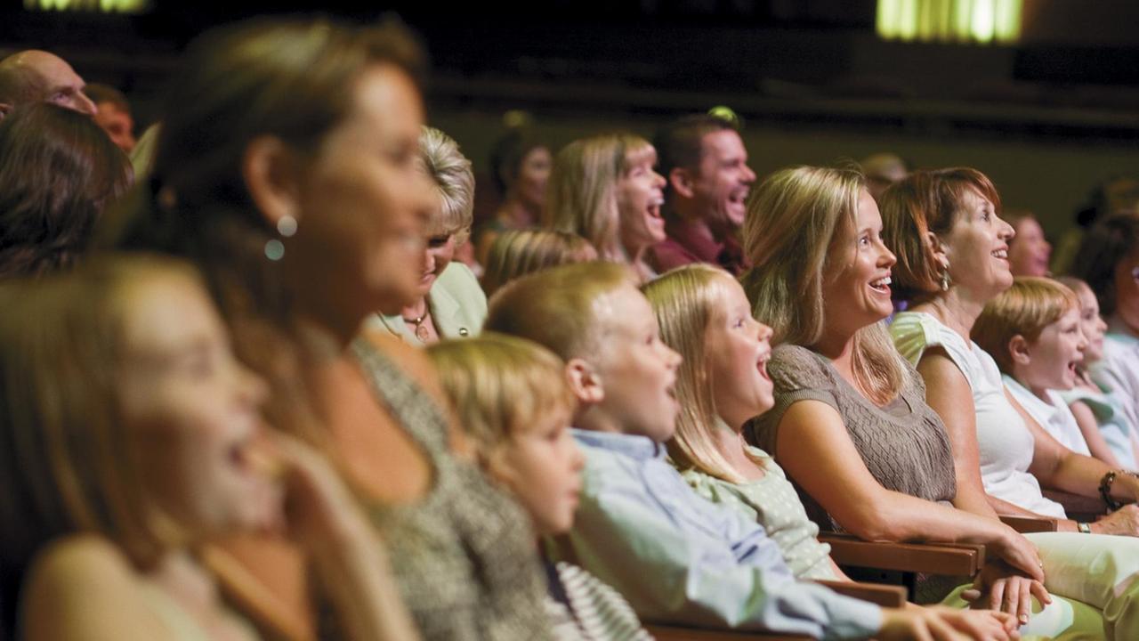 Kinder, Frauen und Männer sitzen vergnügt und lachend in einer Theatervorstellung.