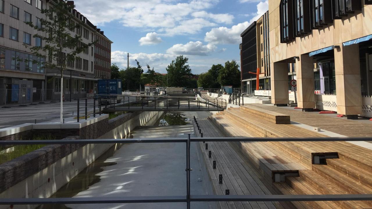 Die Baustelle eines lange Beckens in der Kieler Innenstadt. Am rechten Bildrand sind Sitzplätze zu sehen.