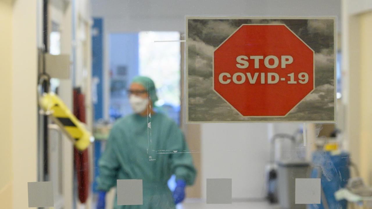 Intensivpfleger laufen in der Corona-Intensivstation des Universitätsklinikums Dresden über den Gang während im Vordergrund ein Schild mit der Aufschrift "Stop Covid-19" an der Tür zu sehen ist.
