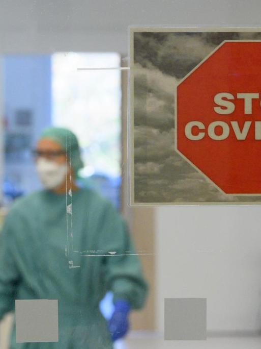 Intensivpfleger laufen in der Corona-Intensivstation des Universitätsklinikums Dresden über den Gang während im Vordergrund ein Schild mit der Aufschrift "Stop Covid-19" an der Tür zu sehen ist.