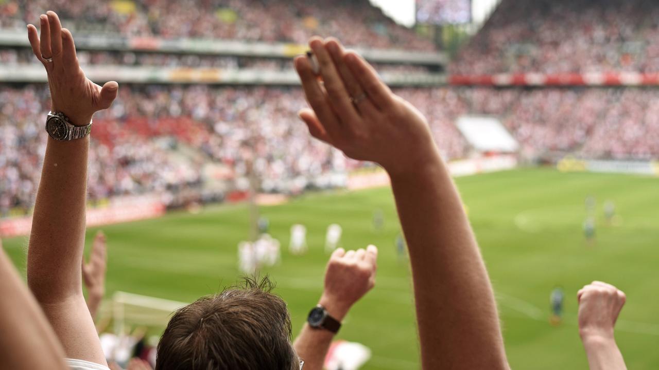 Fußballfans in der Fankurve werfen die Hände in die Luft.