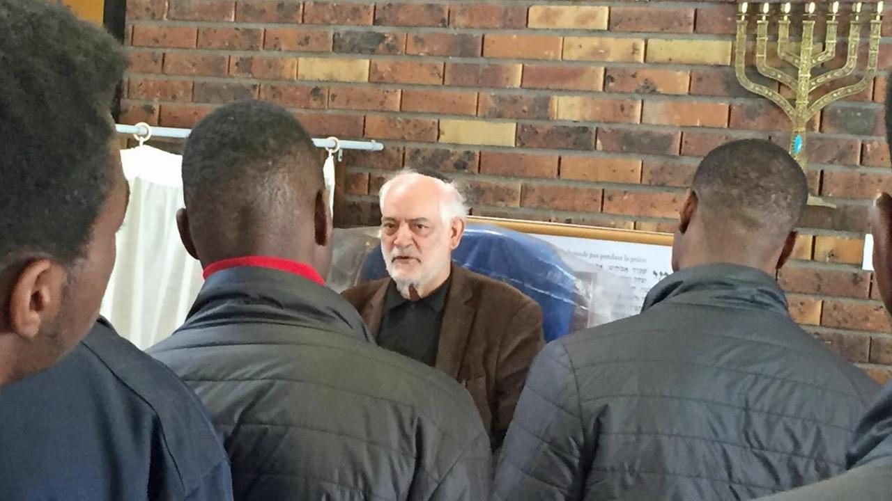 Junge muslimische Männer aus Afrika und der Karibik treffen den Rabbiner Michel Serfaty in der Synagoge und hören ihm aufmerksam zu.