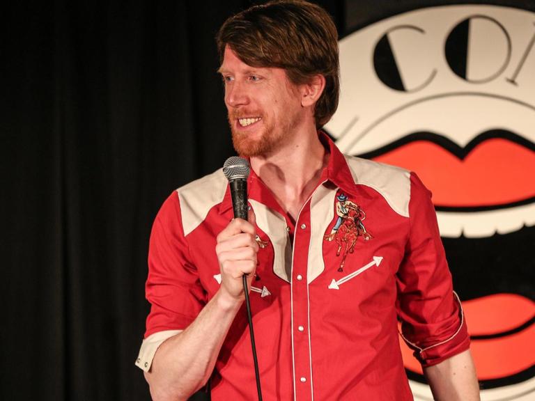 Der Komiker Christian Schulte Loh auf einer Bühne vor dem Logo des renommierten Londoner "Comedy Store"