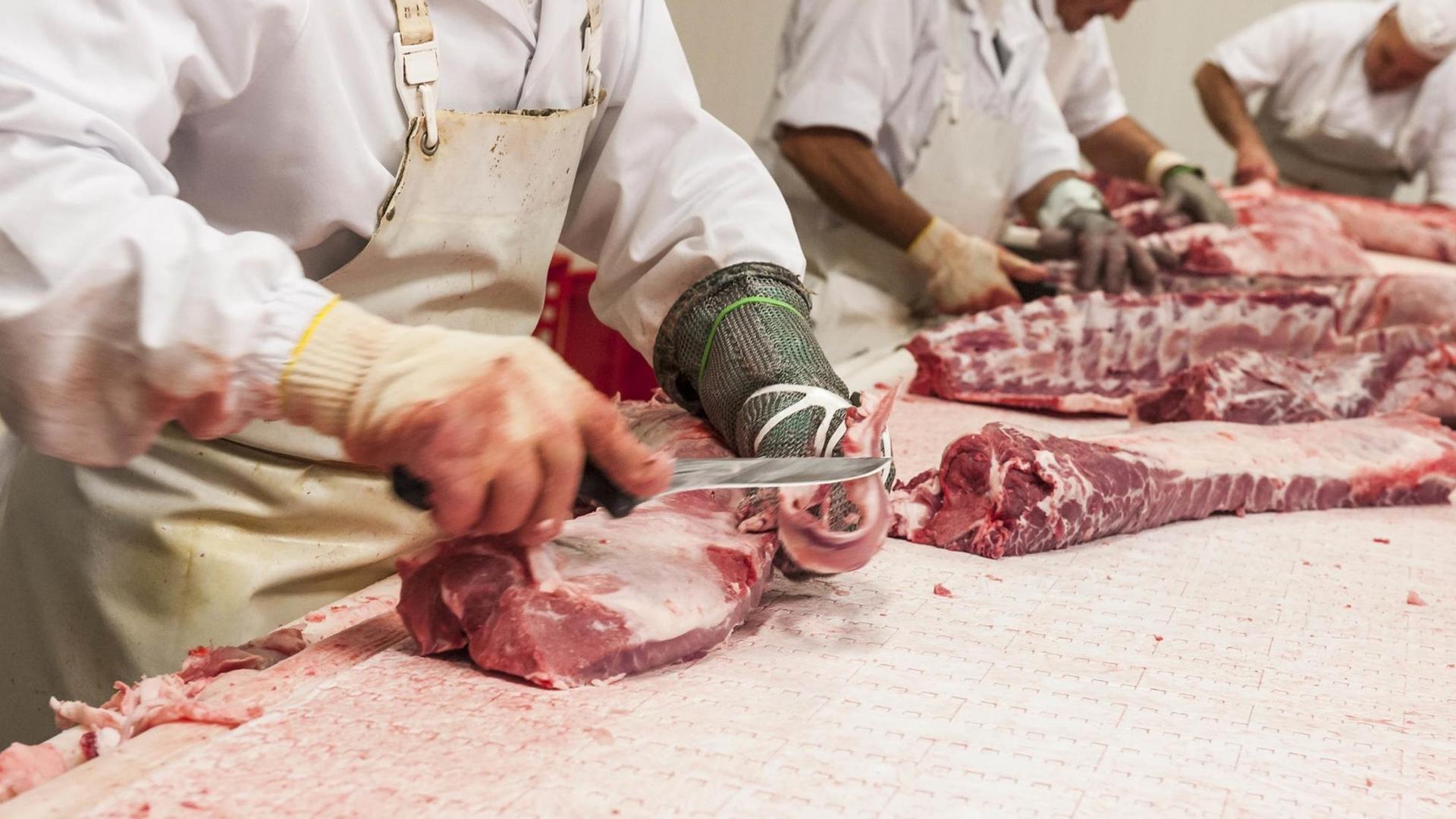Drei Arbeiter bearbeiten Fleisch in einem Schlachthof mit Messern.