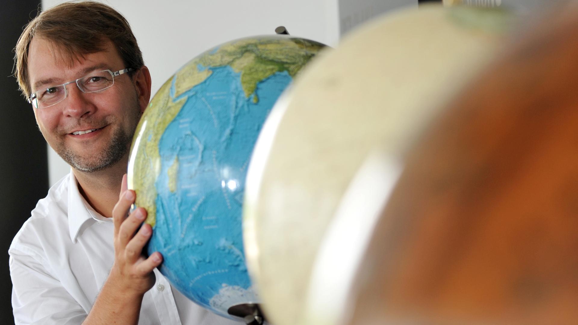 Torsten Oestergaard, Geschäftsführer der Columbus GmbH, steht hinter drei Globen. 