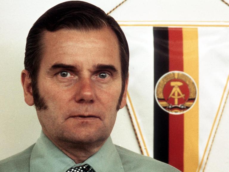 Porträt von Manfred Ewald, dem mächtigsten Mann im DDR-Sport. Im Hintergrund ist die Flagge der DDR zu sehen.