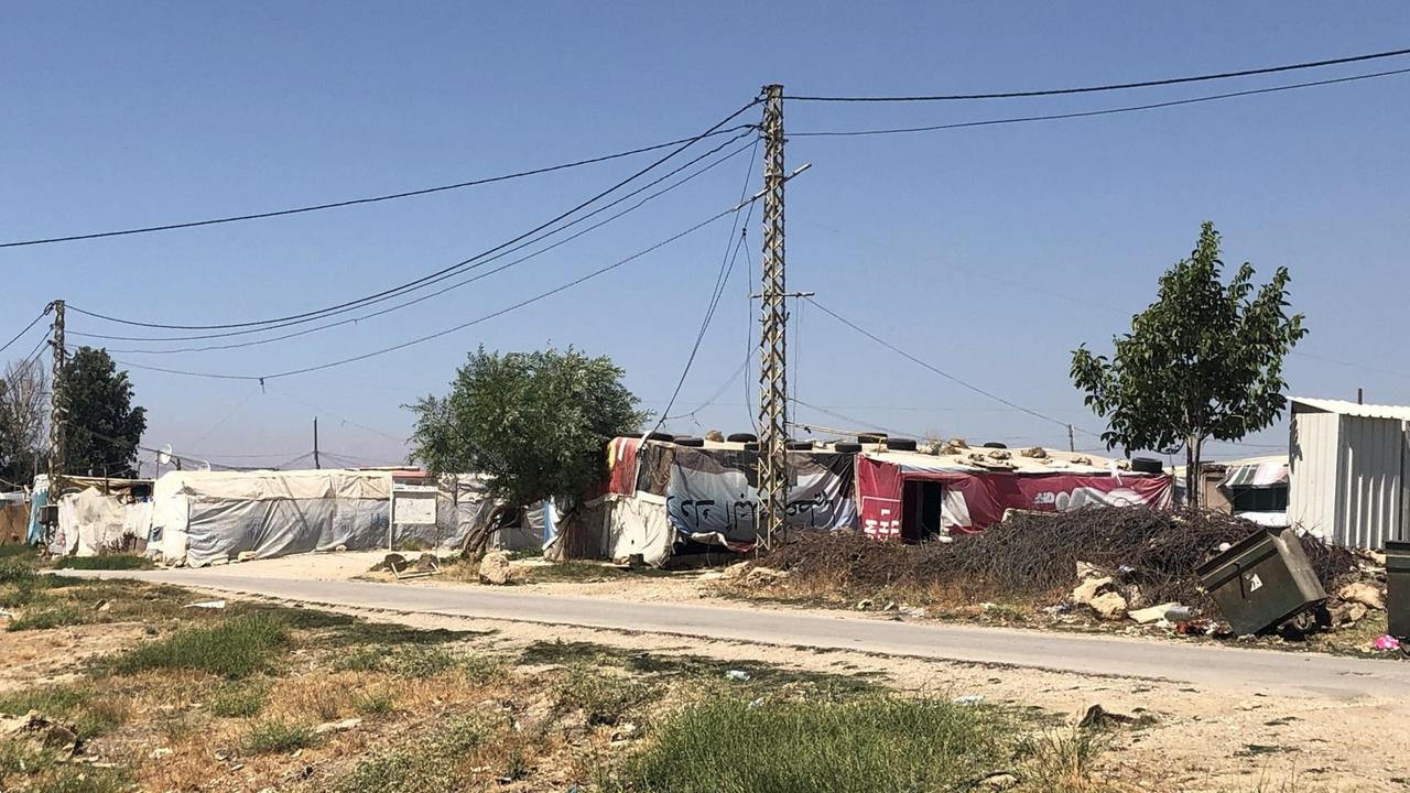 Am Rand einer staubigen Wüstenstraße stehen Zelte und provisorische Baracken.