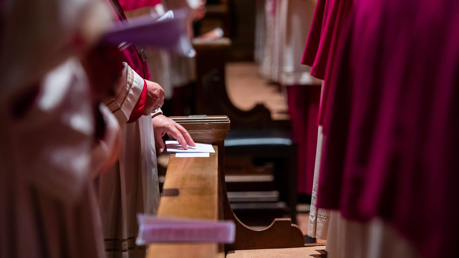 Bischöfe stehen im Gottesdienst in den Kirchenbänken.
