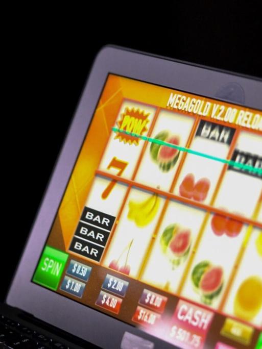 Ein Mann spielt an einem Laptop in einem dunklen Zimmer ein Online-Glücksspiel