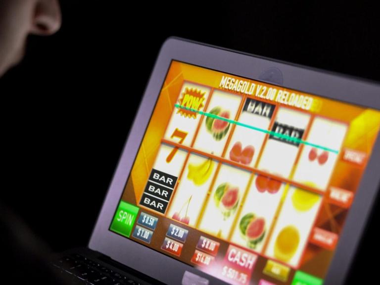Ein Mann spielt an einem Laptop in einem dunklen Zimmer ein Online-Glücksspiel