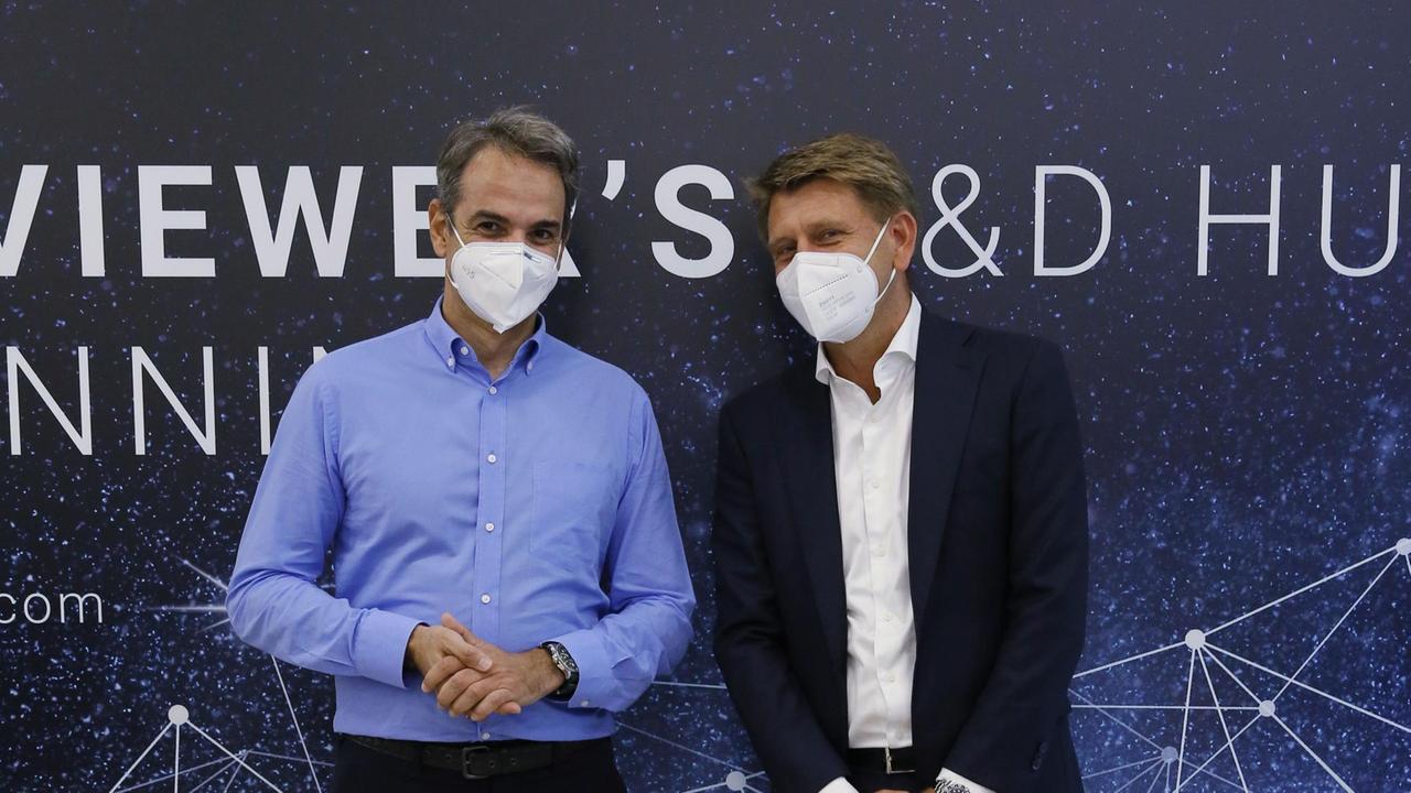 Zwei Männer mit Mundschutz stehen nebeneinander vor einer Werbewand der Firma "Teamviewer".