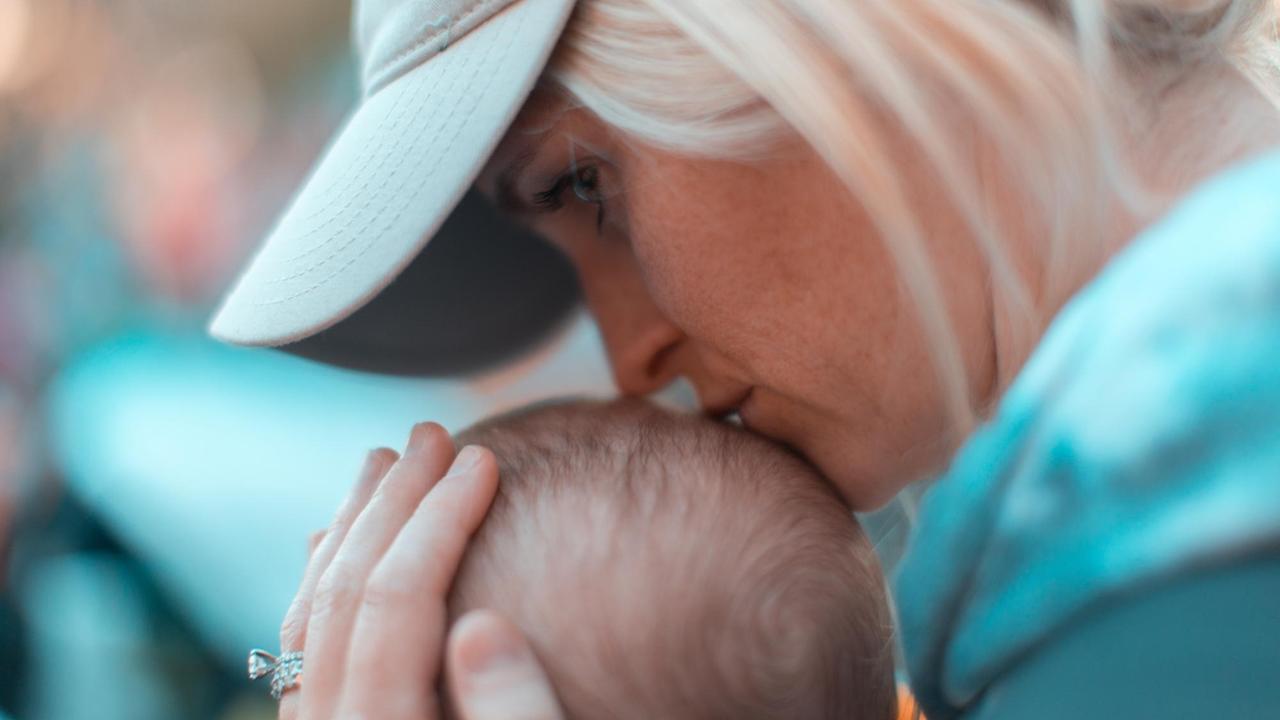 Eine nicht mehr ganz junge Mutter küsst liebevoll den Kopf Ihres Babies.
