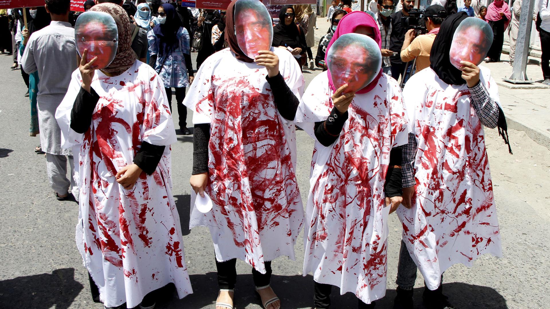 Vier Frauen tragen bei einer Demonstration in Kabul Masken, die das blutverschmierte Gesicht von Farkhunda Malikzada zeigen