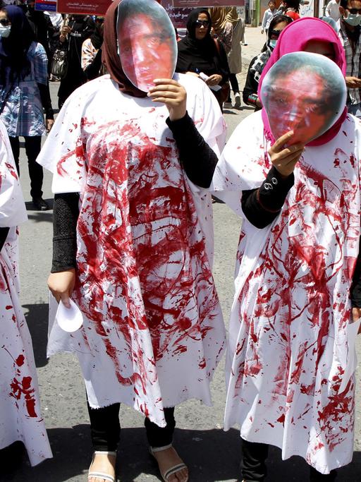 Vier Frauen tragen bei einer Demonstration in Kabul Masken, die das blutverschmierte Gesicht von Farkhunda Malikzada zeigen