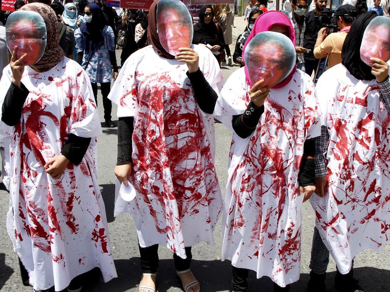 Vier Frauen tragen bei einer Demonstration in Kabul Masken, die das blutverschmierte Gesicht von Farkhunda Malikzada zeigen