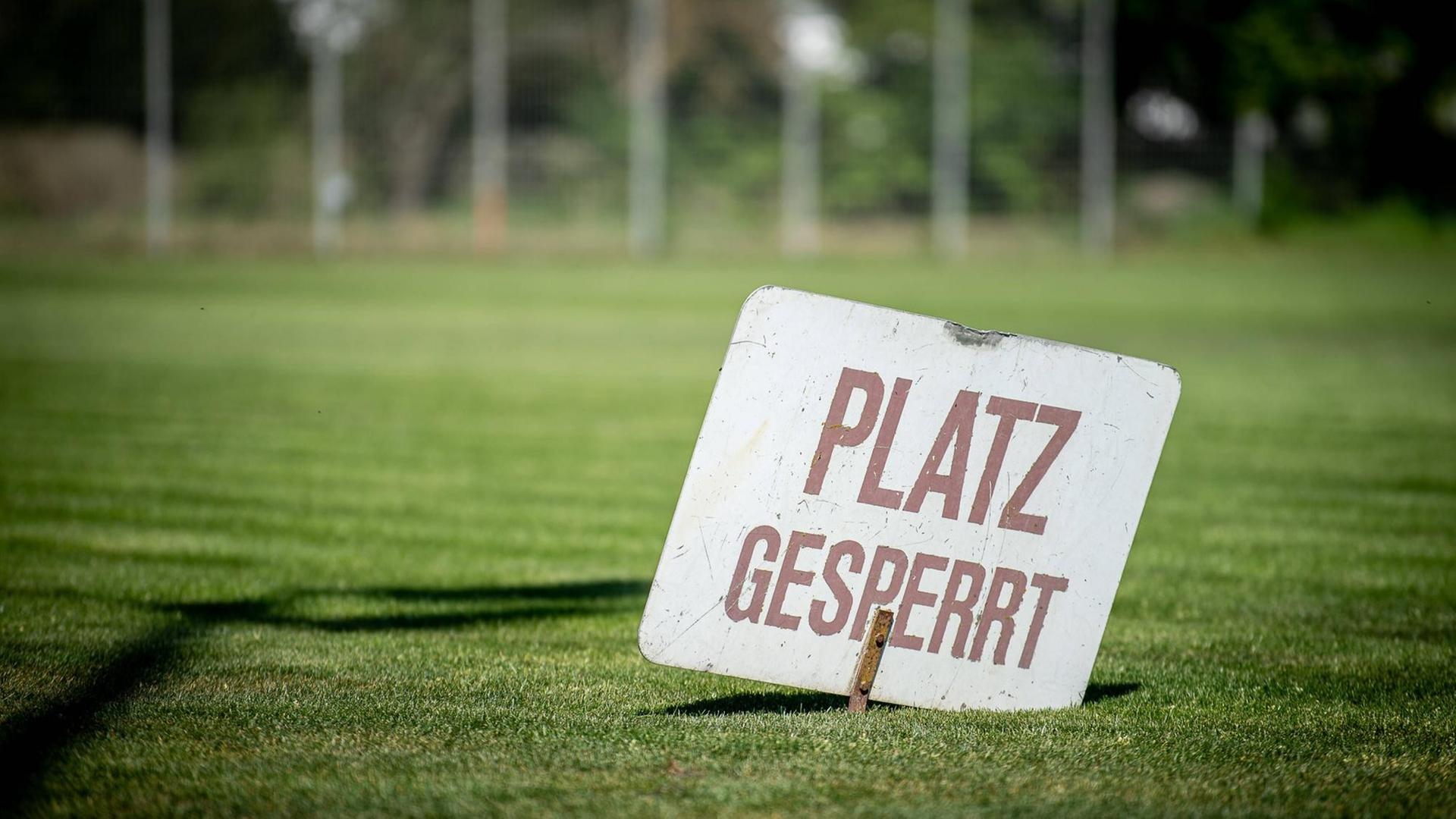 Ein Schild mit der Aufschrift "Platz gesperrt" steckt im Rasen eines Vereinsspielfeldes.