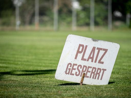 Ein Schild mit der Aufschrift "Platz gespresst" steckt im Rasen eines Vereinsspielfeldes
