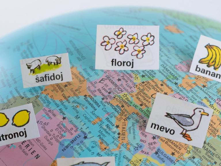 Auf einem Atlas, der Europa und einen Teil Afrikas zeigt, sind mehrere Zettel mit Esperanto-Wörtern verteilt