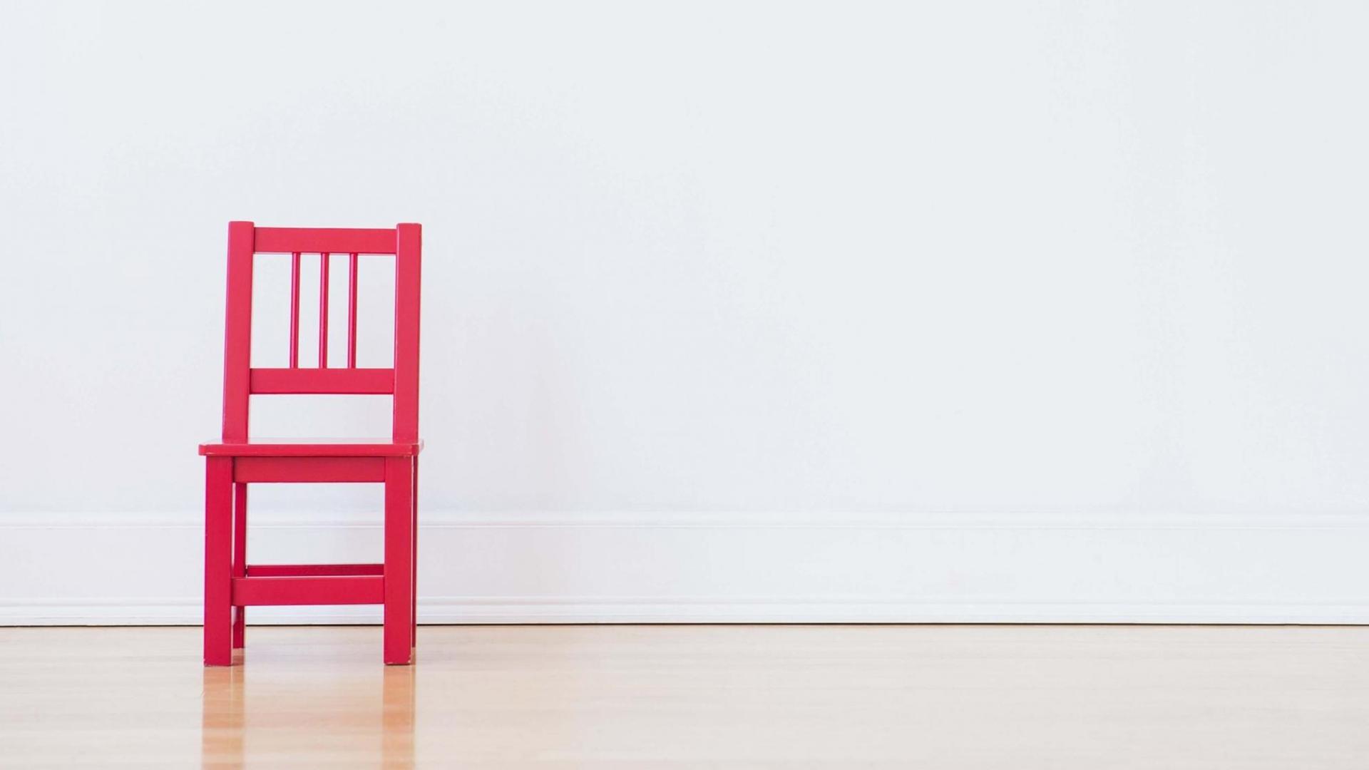 Ein roter Stuhl steht in einem leeren Raum.