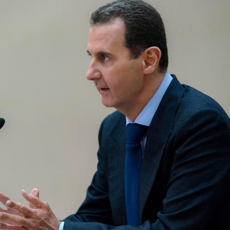 Der syrische Machthaber al-Assad sitzt vor einem Mikrofon.