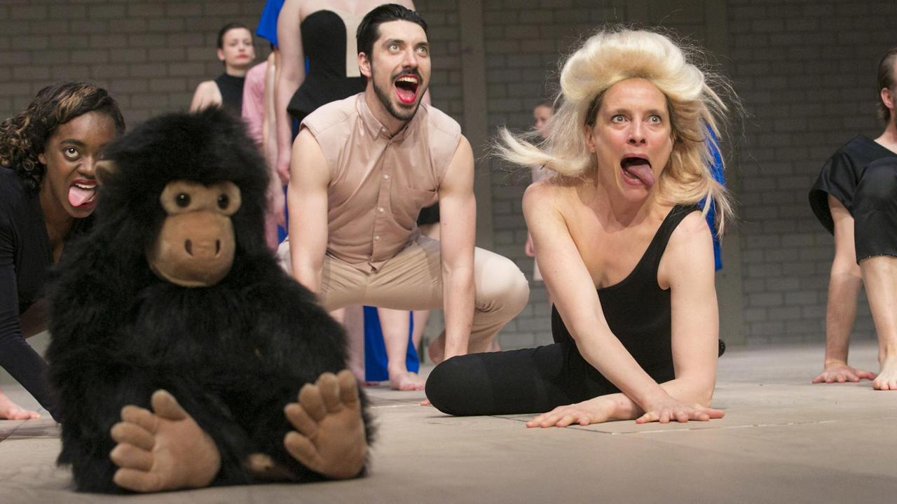 Performer auf der Bühne, dort sitzt auch ein Plüschaffe, die ihre Zunge herausstrecken.