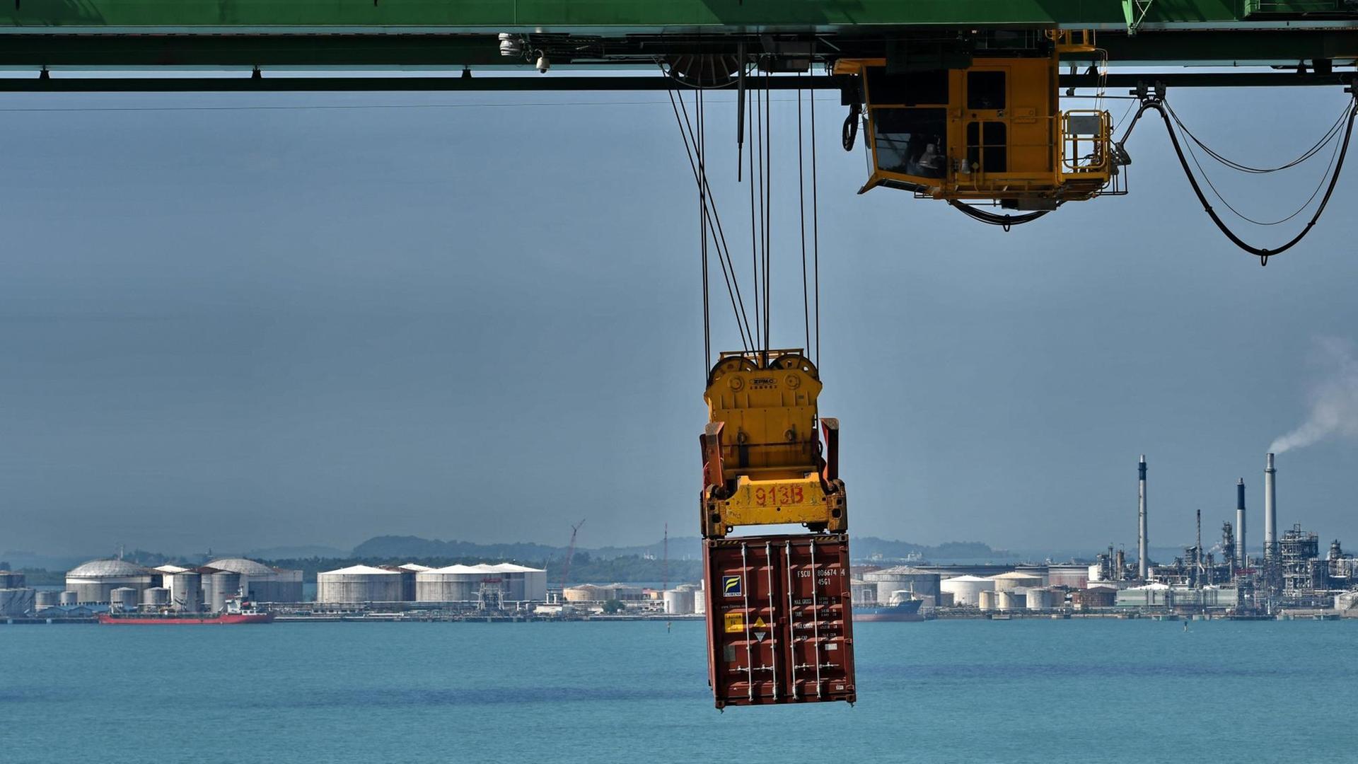 Ein Container schwebt am Verladekran über dasa türkisblaue Meer vor Singapur.