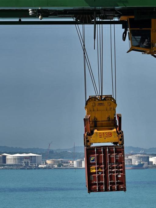 Ein Container schwebt am Verladekran über dasa türkisblaue Meer vor Singapur.