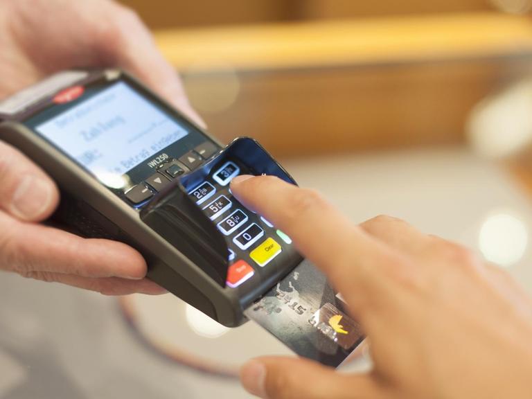 Eine Person bedient ein Lesegerät zur elektronischen Zahlung mit EC- oder Kreditkarte.