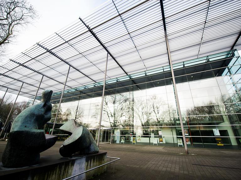 Halle der Ruhrfestspiele in Recklinghausen, Blick vom Boden auf ein Glasgebäude, im Vordergrund eine Skulptur