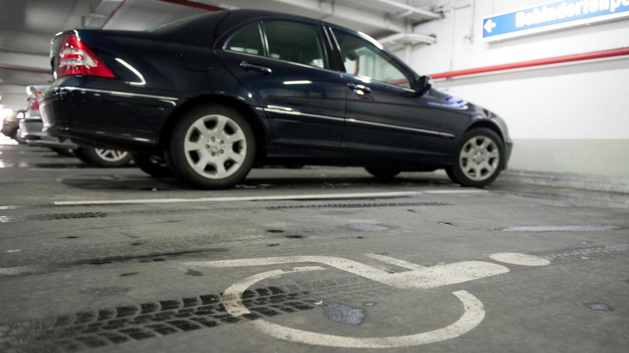 Das Auto ist schwarz; der Behindertenparkplatz ist duch ein großes Rollstuhlfahrer-Symbol auf dem Boden gekennzeichnet.