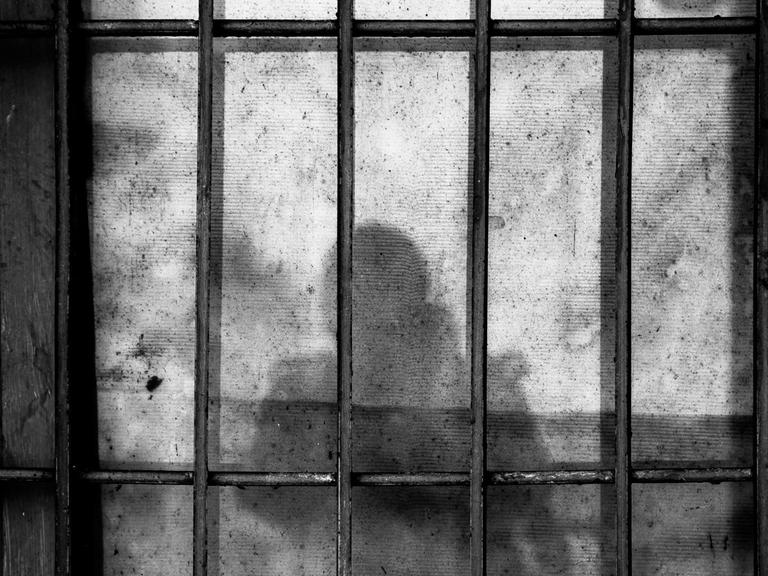 Der Schatten von einem Menschen mit Kind auf dem Arm vor Gefängnisgittern.