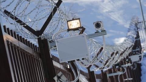 Ein massiver Zaun am olympischen Bergdorf Derevnya in Russland mit Scheinwerfer und Kamera.