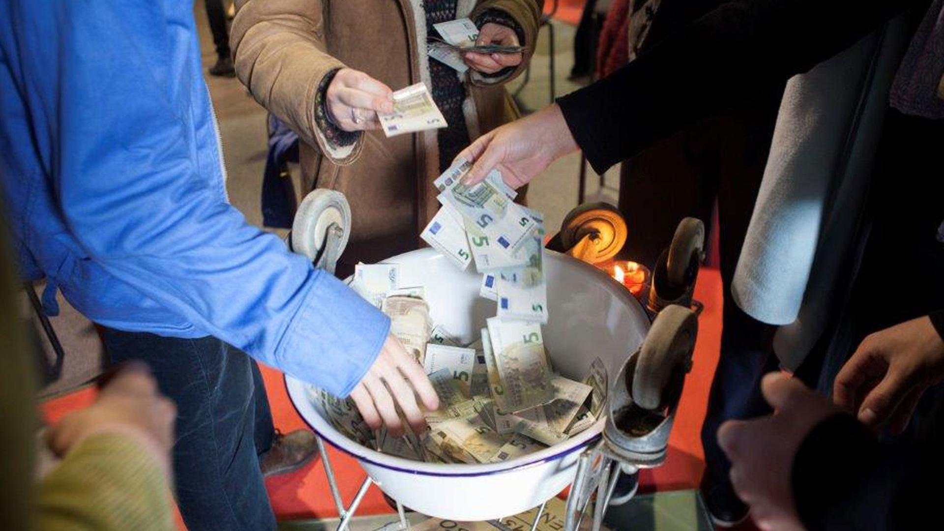 Menschen werfen Geldscheine in eine Schale.