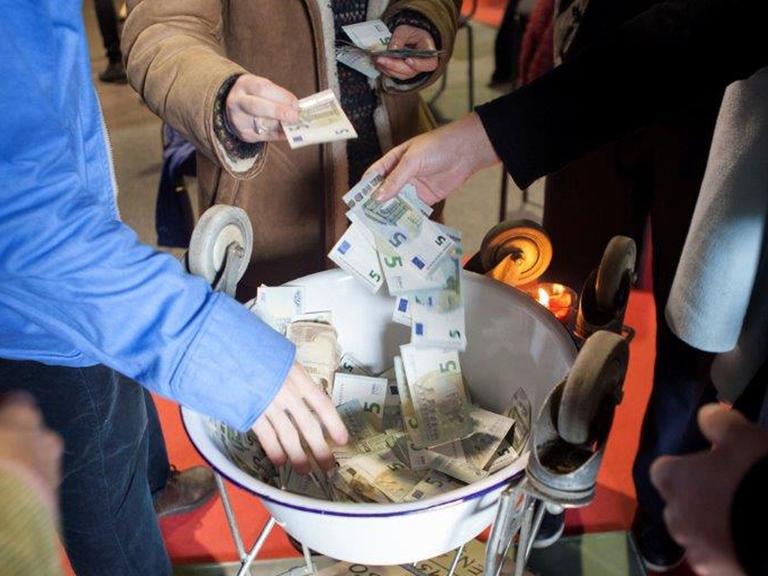 Menschen werfen Geldscheine in eine Schale.
