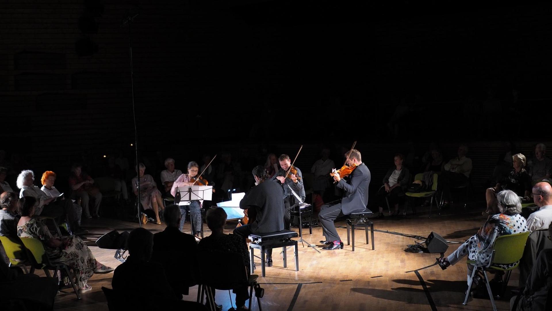 Ein Streichquartett spielt mitten im Saal, umgeben von Publikum und beleuchtet von einem Spotlight.