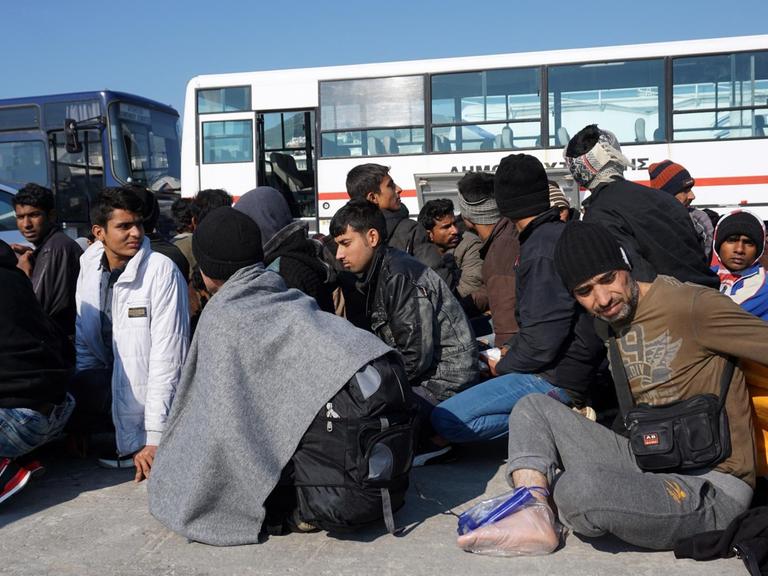 Sie sehen Flüchtlinge auf der griechischen Insel Lesbos. Im Hintergrund sehen Sie Busse.