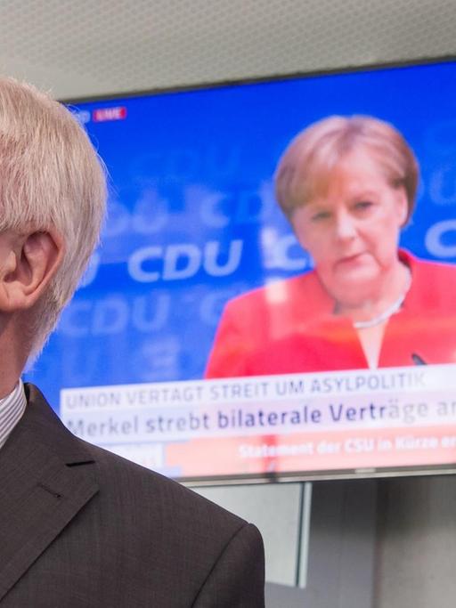 Horst Seehofer, CSU-Vorsitzender und Bundesminister für Inneres, Heimat und Bau, läuft auf seinem Weg zu einer Pressekonferenz, die in Anschluss an die Sitzung des CSU-Vorstands stattfindet, an einem Fernseher vorbei, auf dem die Pressekonferenz von Bundeskanzlerin Angela Merkel (CDU) übertragen wird.