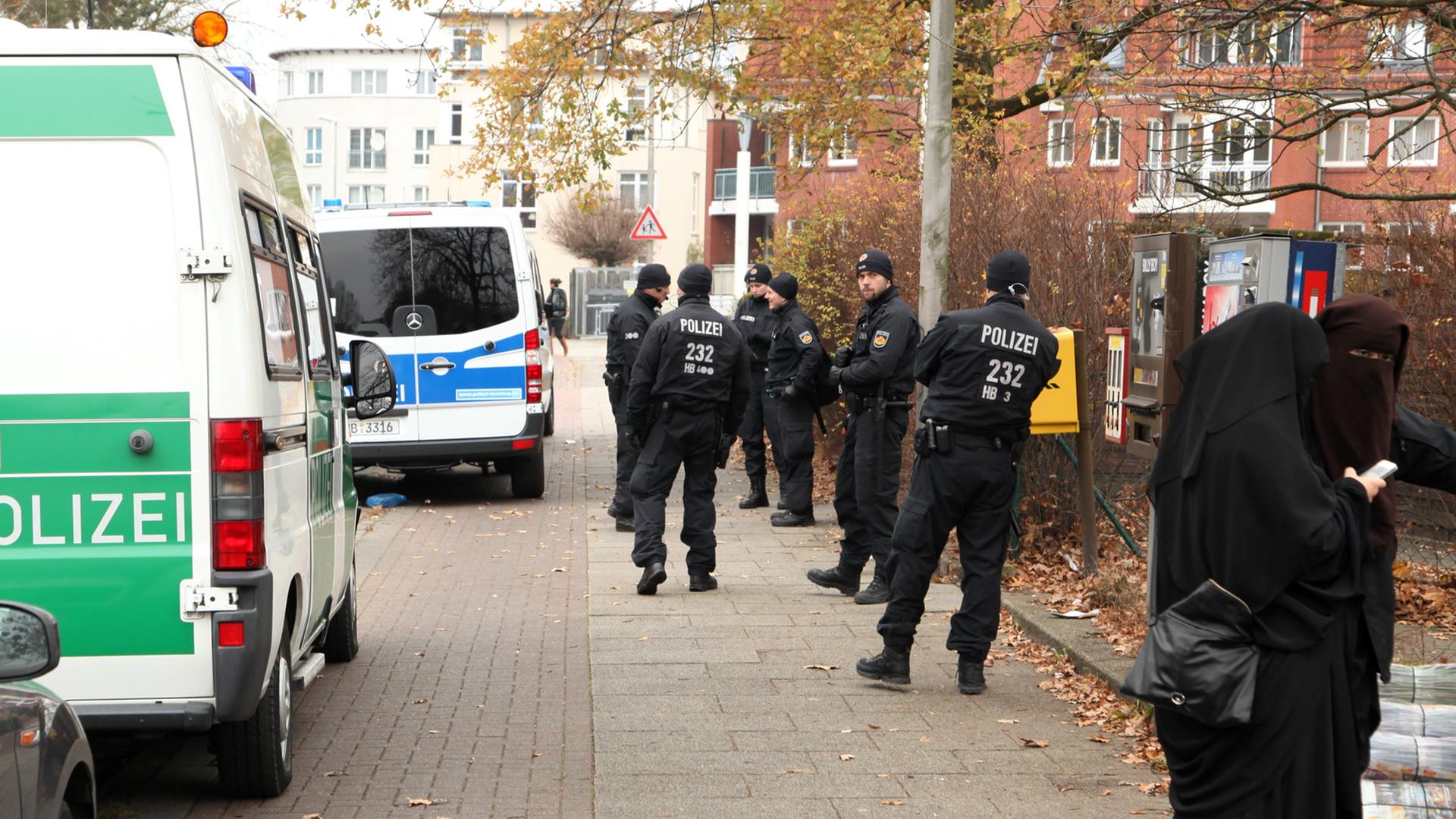 Polizeiwagen und Beamte stehen in Bremen während einer Durchsuchung vor dem salafistischen Kultur & Familien Verein (KuF) im Stadtteil Gröpelingen neben zwei Frauen, die vollkommen verschleiert sind.