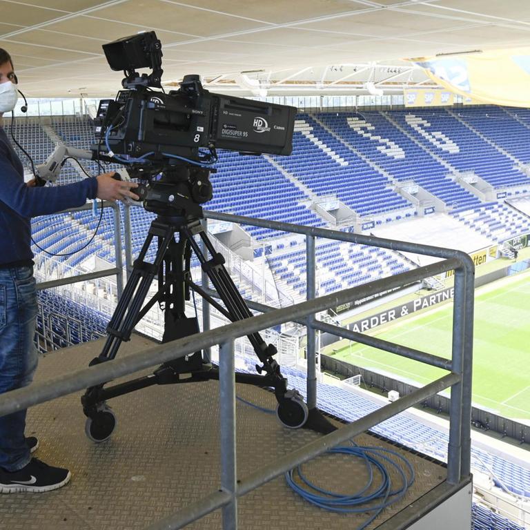 Ein Kameramann trägt im Stadion hinter seiner Fernsehkamera eine Mund-Nasen-Maske.