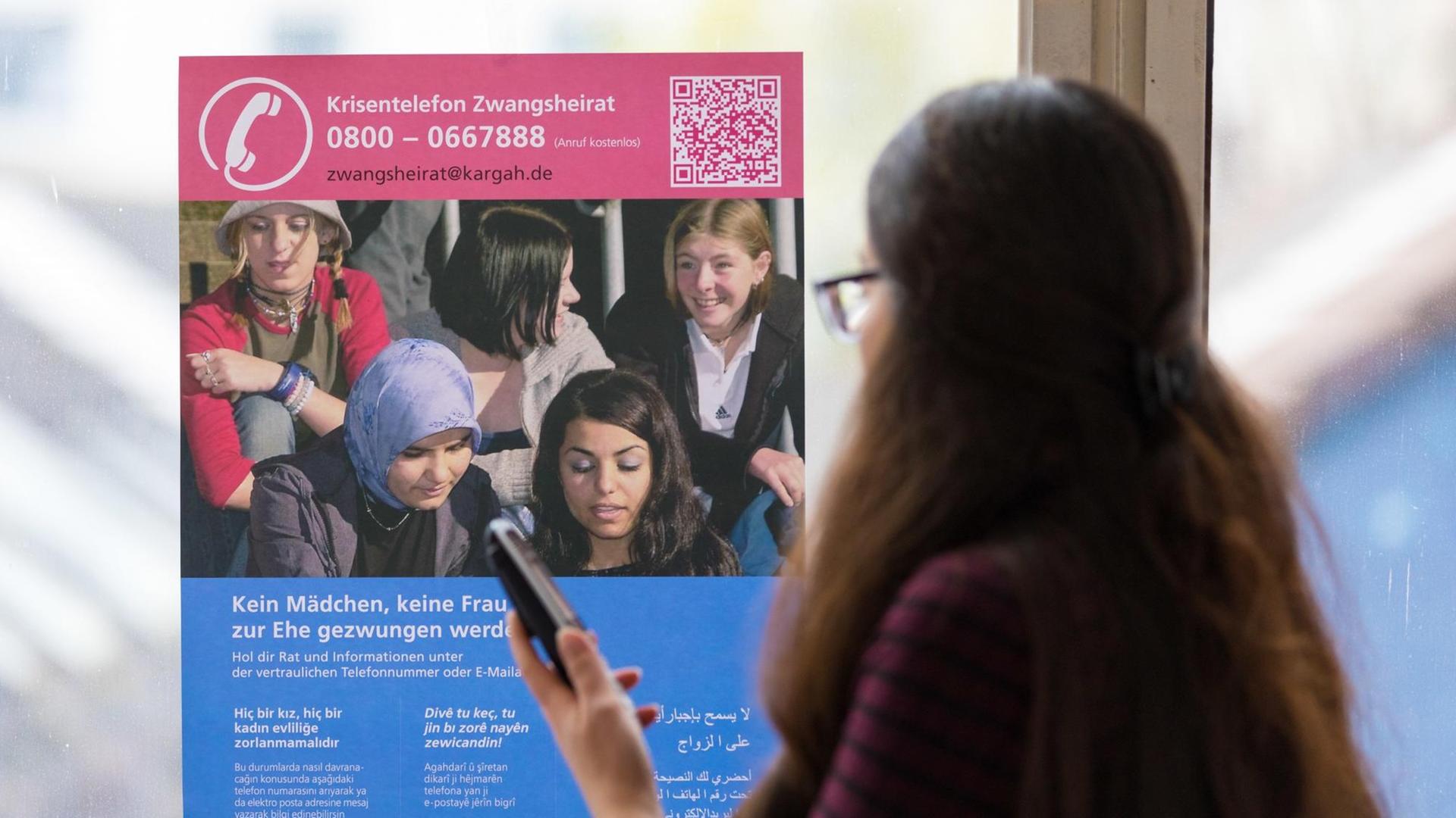 Eine Mitarbeiterin des niedersächsischen Krisentelefons sitzt mit einem Telefon in der Hand vor einem Plakat des Krisentelefons gegen Zwangsheirat.