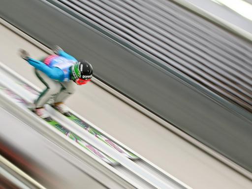 Ein Skispringerin fährt eine Schanze hinab