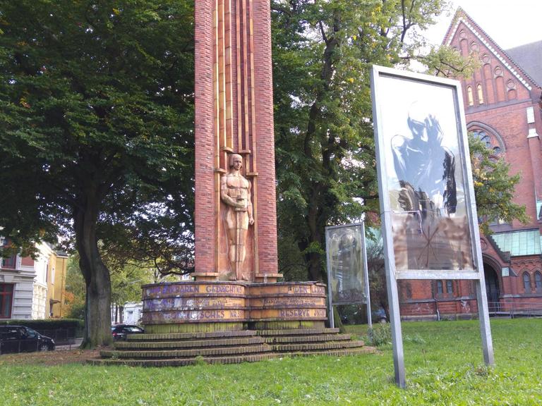 Das Kriegerdenkmal aus den 1920er Jahren auf dem Vorplatz der St. Johanniskriche in Hamburg Altona. Heute ist es umstellt von drei großen auf Plexiglas fixierten Zeichnungen, die Opfer des Krieges symbolisieren sollen.