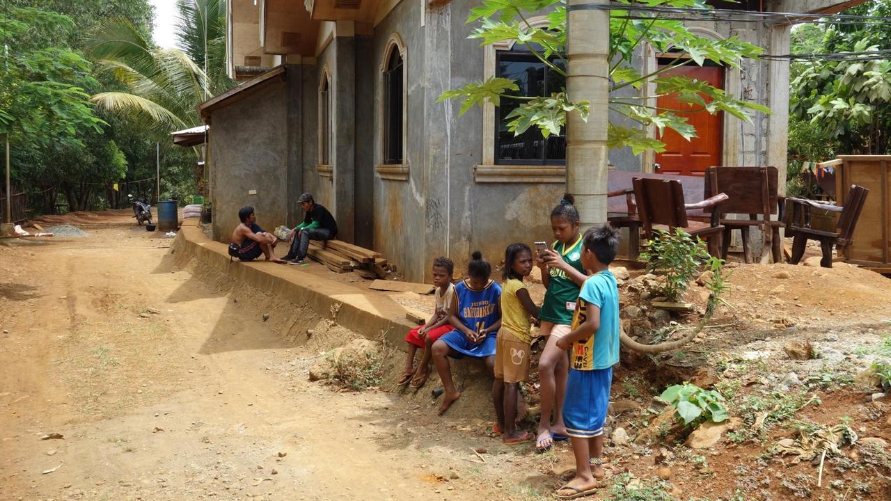 Vor einem der Betonhäuser von Punta Negra sind Kinder zu sehen - zwei davon beschäftigen sich mit ihren Smartphones. (Foto: Thomas Kruchem) 